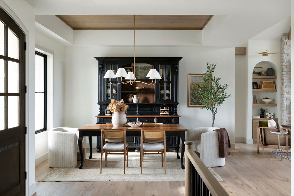 Modern Farmhouse dining room furnished with a family heirloom hutch, 2 accent end chairs, a black and wooden dining table, and 4 dining chairs. The seating arrangement lays on top of a cream vintage rug. Located in Independence, Minnesota. Design by O'Hara Interiors.