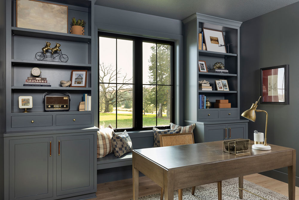 An office with two bookshelves on both sides of a large window, color drenched in a dark gray paint with blue undertones. This same paint is color drenched throughout the room.  Located in Independence, Minnesota. Designed by O'Hara Interiors. 